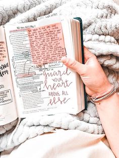 a person holding an open book on top of a blanket with writing on the pages