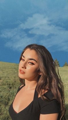 a woman standing in the grass with her eyes closed and looking off into the distance