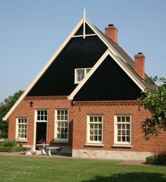 a black and red brick house sitting on top of a lush green field