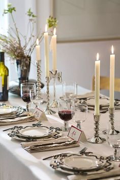 a table set with place settings and wine glasses, candles and flowers in vases