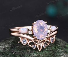 a ring with an oval pink stone surrounded by white diamonds on top of a rock