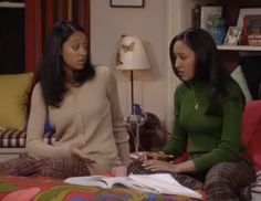 two women sitting on a bed talking and looking at something in front of the camera