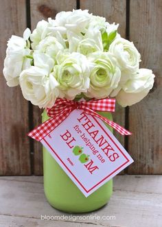 a green vase filled with white flowers on top of a wooden table next to a sign