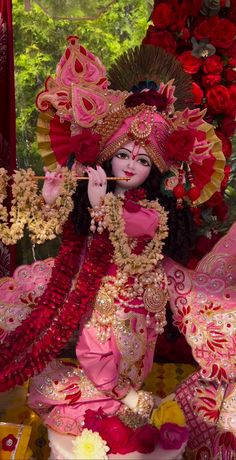 a statue of a woman in pink and red with flowers on the ground behind her