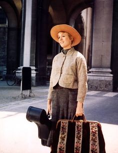 a woman holding a suitcase and wearing a hat