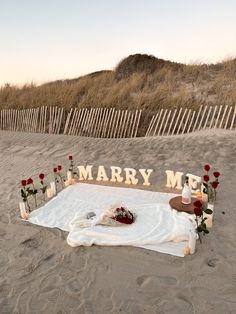 a sign that says marry me on the beach with flowers and candles in front of it