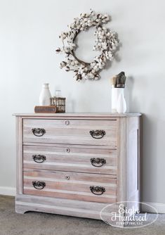 an old dresser is painted white and has a wreath on the wall above it, along with other items