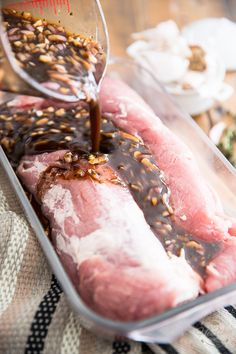 someone pouring sauce on raw meat in a plastic container with other food items around it