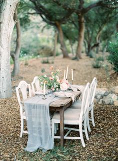 the table is set with white chairs and flowers on it, along with candles in vases