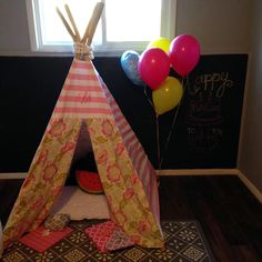 a teepee tent with balloons on the floor in front of a chalkboard wall