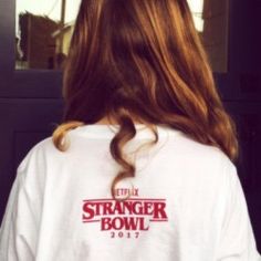 a woman with long hair wearing a white t - shirt that reads netflix's stranger bowl