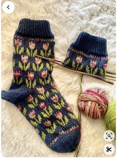 a pair of blue socks with flowers on them next to a ball of yarn and knitting needles