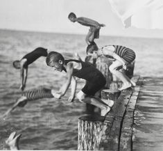 three boys jumping into the water from a pier in an old black and white photo