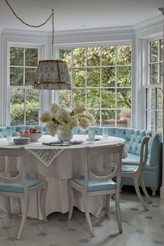 a dining room table with blue chairs and white flowers in vases on the table