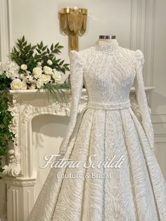 a white wedding dress on display in front of a fireplace with flowers and greenery