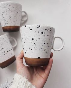 a hand holding a white and brown coffee cup with black speckles on it