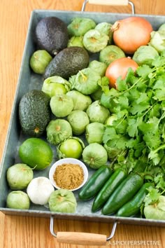 an assortment of vegetables are displayed in a tray on a wooden table, including avocados, tomatoes, cucumbers and green beans