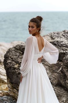 a woman in a white dress standing on rocks near the ocean with her back to the camera