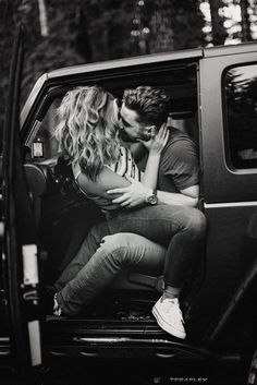 black and white photo of couple kissing in the back of a truck with trees behind them