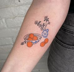 a person with a tattoo on their arm holding a bowl of oranges and flowers