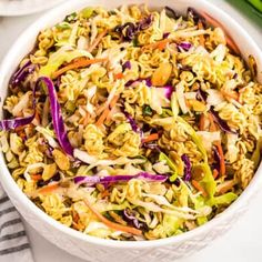 a bowl filled with noodles and vegetables on top of a white table next to green onions