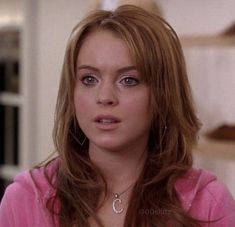 a close up of a person with long hair and wearing a pink shirt in a room