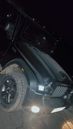 the front end of a black jeep parked in a parking lot at night with its lights on