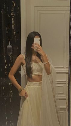 a woman taking a selfie in front of a mirror wearing a white crop top and skirt