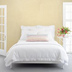 a bed with white linens and pillows in a yellow room next to an open door