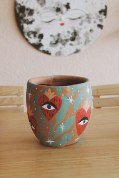 a cup sitting on top of a wooden table next to a wall with a cat face painted on it