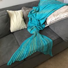 a gray couch with a blue mermaid tail blanket on it's back and two white pillows