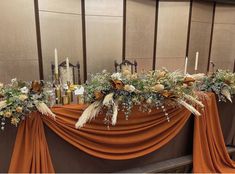 an arrangement of flowers and candles on top of a table with orange draping