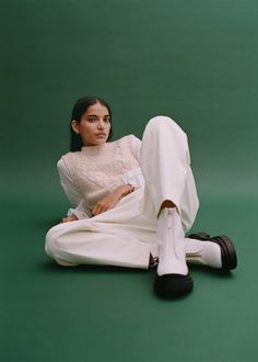 a woman sitting on the ground with her legs crossed wearing white pants and a sweater