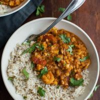 two bowls filled with rice and curry on top of a wooden table next to a spoon