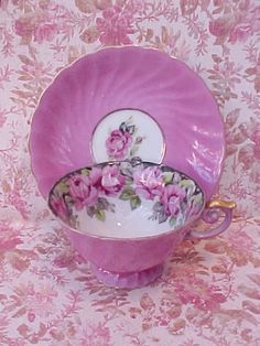 a pink cup and saucer sitting on top of a floral tablecloth with gold trim