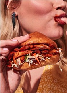 a woman taking a bite out of a sandwich with bacon on it's bun