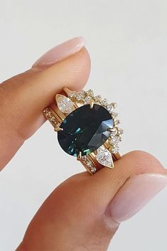 a woman's hand holding a ring with an oval blue stone surrounded by small diamonds