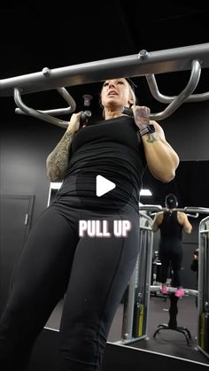 a woman in black shirt and leggings doing pull up on a gym machine