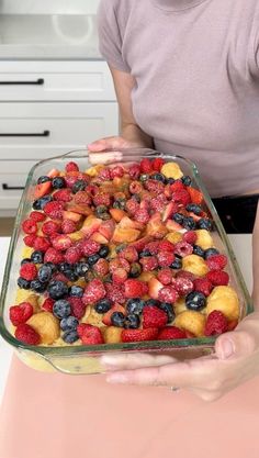 a person holding up a casserole dish full of berries and strawberries in the kitchen