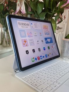 an open laptop computer sitting on top of a white desk next to a vase with flowers