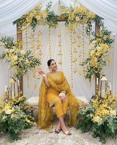 a woman in yellow sitting on a bench with flowers and greenery around her feet