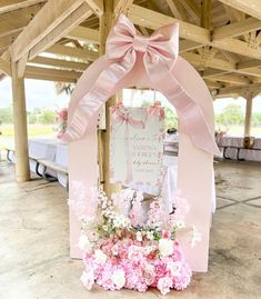 a pink and white wedding arch with flowers on the ground in front of a sign