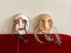 two masks sitting on top of a red velvet table next to each other with long hair