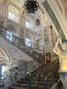 an ornate staircase with statues and chandelier in a large white walled building that has intricately painted walls