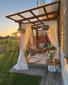 a patio covered in white drapes next to a wooden table with flowers on it