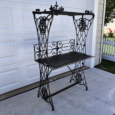 a wrought iron bench sitting in front of a garage door with a white house behind it