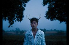 a man with horns on his head standing in front of trees