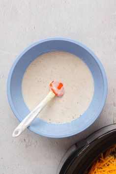 a bowl of cheese soup with a spoon in it next to a container of shredded cheese