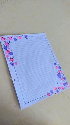 a piece of lined paper with pink and purple flowers on it sitting on a table