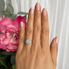 a woman's hand with a diamond ring on her finger and pink flowers in the background